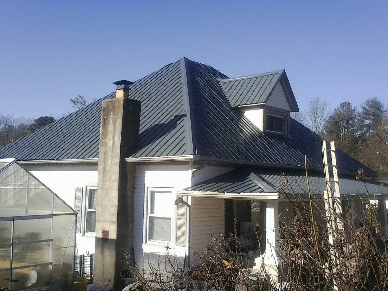 Dark blue standing seam metal roof on a white farmhouse with dormer — Slate & Tile Roof Repair by Roofing Brothers in Munford