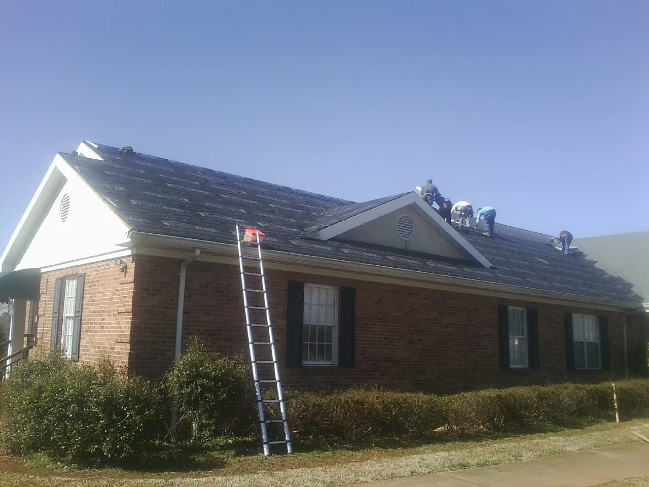 Crew tearing shingles off a brick ranch roof with a ladder set — Metal Roof Repair work by our crew in Munford