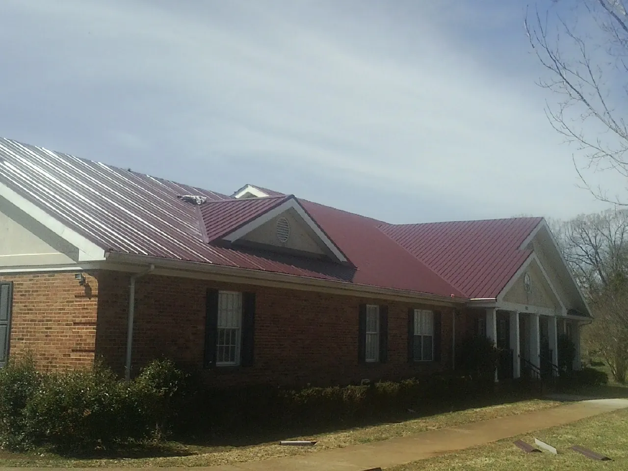 Red metal roof with gabled entries on a long brick building, from a Hail Damage Roof Repair job in Munford
