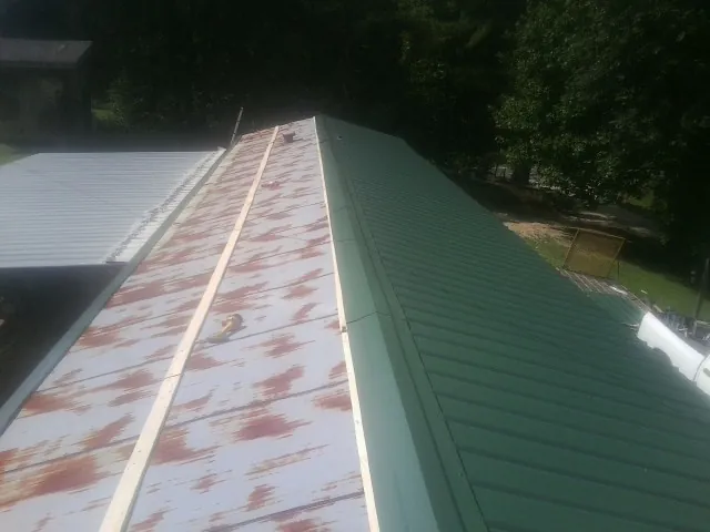 Old rusted panels beside newly installed green metal roofing — Wind Damage Roof Repair by Roofing Brothers in Munford