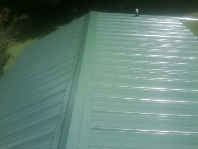New green metal panels meeting at the ridge of a roof — Flat Roof Repair work by our crew in Munford