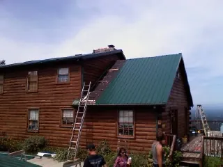 Green metal roof going on a two story log home with ladders set in Munford