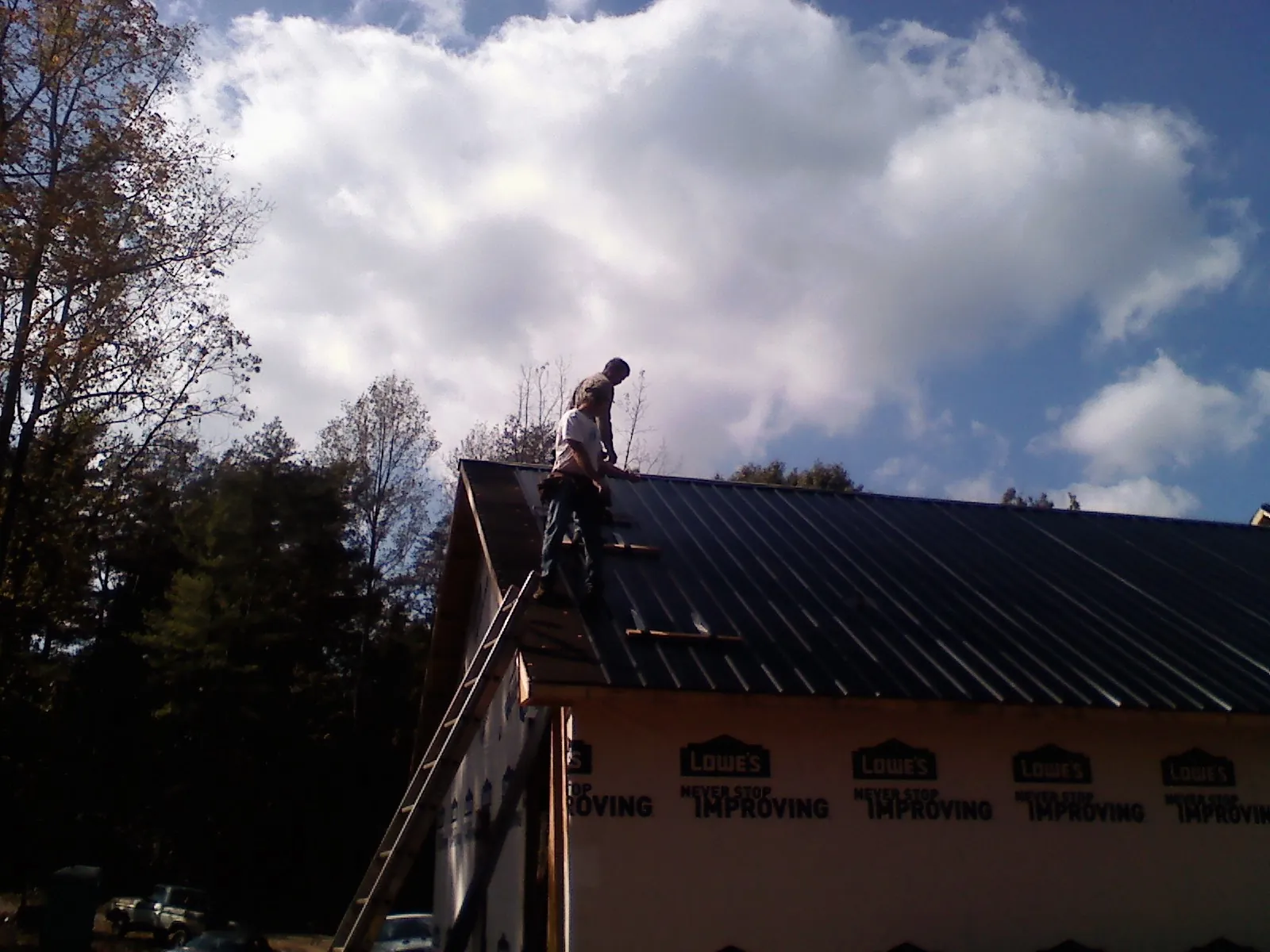 Roofer fastening dark metal panels high against a cloudy sky, from a Roof Inspection job in Munford