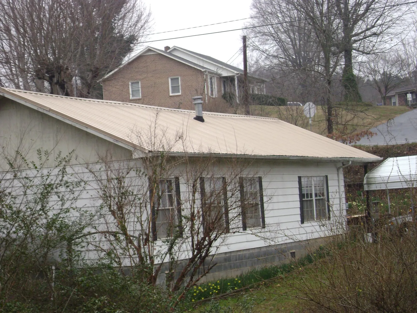 Tan metal roof on a white sided house set into a hillside — Commercial Roofing by Roofing Brothers in Munford
