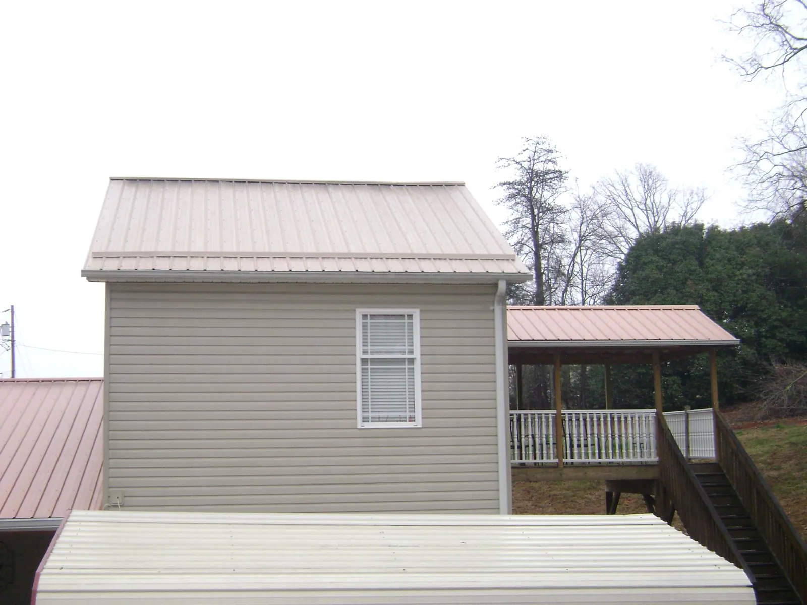 Tan metal roofs on a two story addition and attached porch, from a Roof Replacement job in Munford